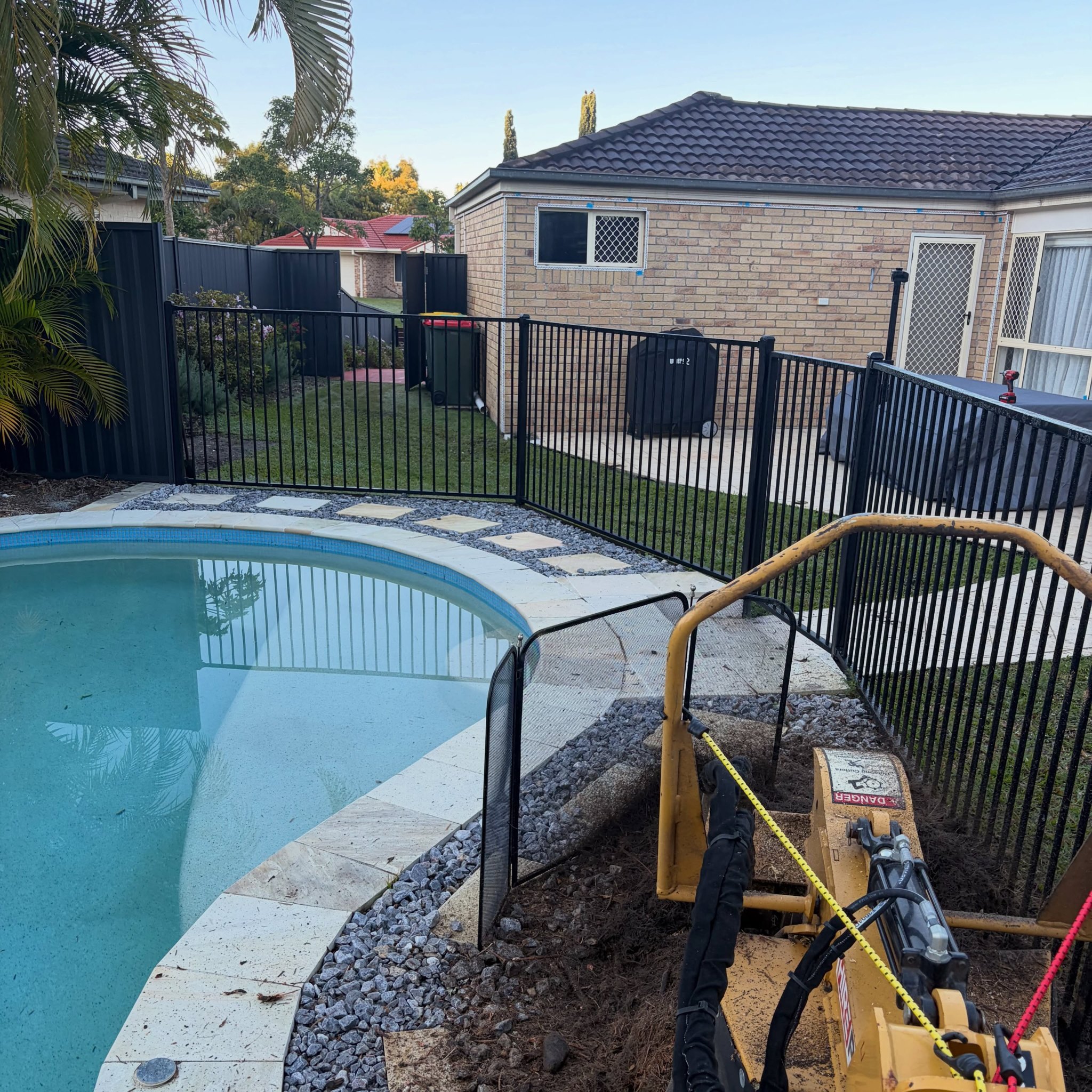 Stump grinder working beside a pool fence in a backyard